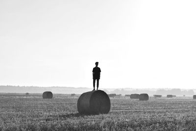 Full length of man standing on hay bale against sky