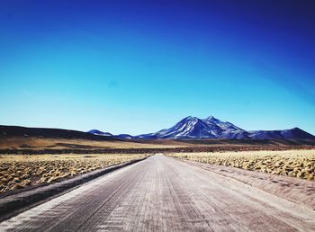 Empty road in desert against clear blue sky