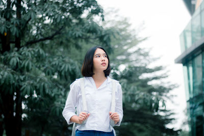 Portrait of beautiful young woman standing against trees