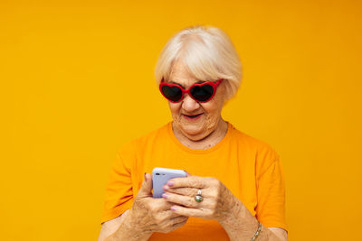 Senior woman using mobile phone against yellow background