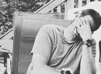 Smiling man covering face with hand while sitting on chair