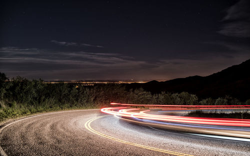 Light trails on road against sky at night