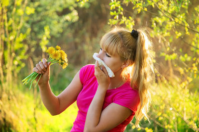 Woman holding flowers blowing nose with tissue paper in garden