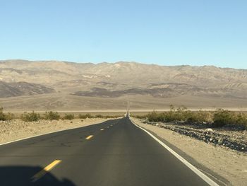 Road leading towards mountains against clear sky