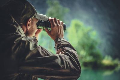 Man looking through binoculars against tree