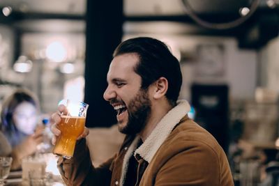 Man holding beer glass laughing while sitting in restaurant