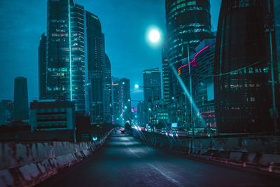 Illuminated street amidst buildings against sky at night