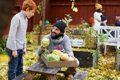 Man talking to boy while holding cabbage at table in yard