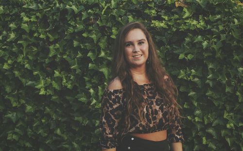 Portrait of smiling young woman standing against plants