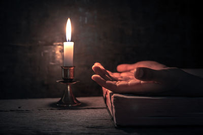 Hand holding lit candle in the dark