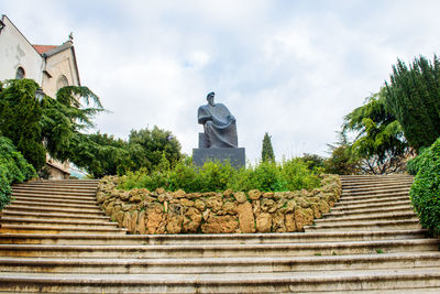 Low angle view of statue against trees and building against sky