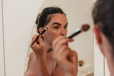 Mirror photo of beautiful young woman putting on makeup