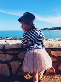 Rear view of girl looking away while standing by sea against sky