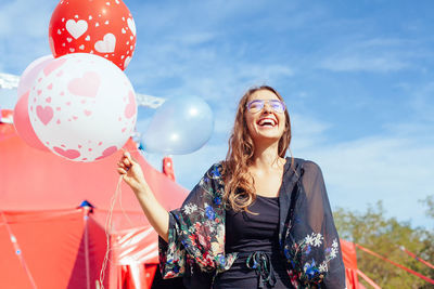 Smiling young woman holding balloons against sky