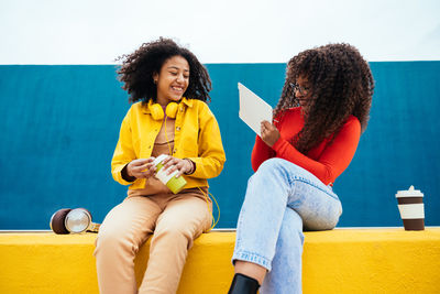 Happy female friends sitting on retaining wall