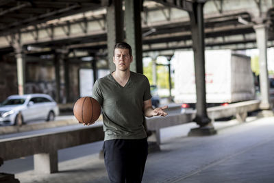 Portrait of young man with basketball standing on bridge