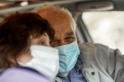 An elderly senior couple in medical face mask driving a car.  travel and old people concept