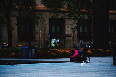 People sitting on street against building in city