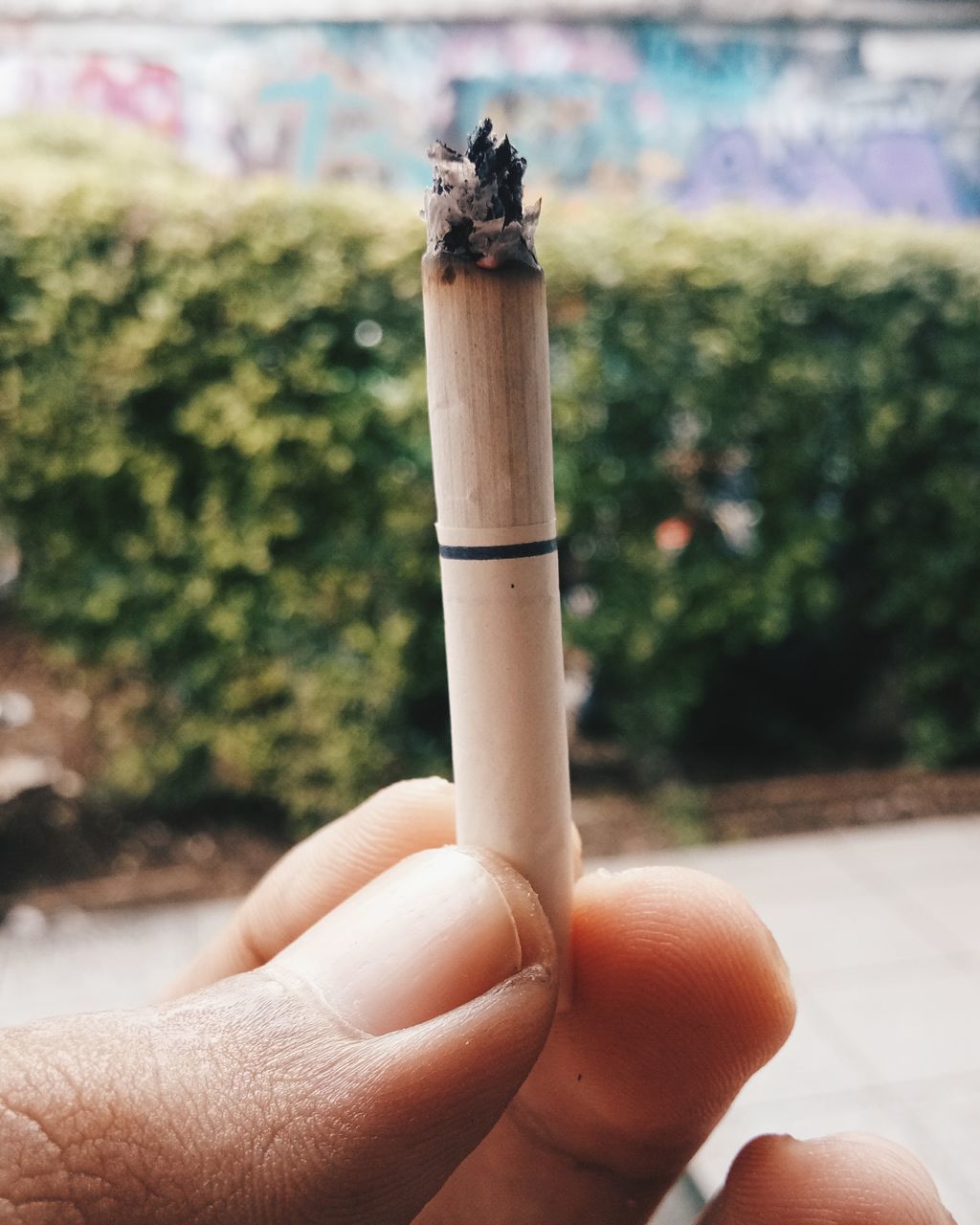 CLOSE-UP OF HAND HOLDING CIGARETTE AGAINST BLURRED BACKGROUND