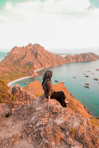 Man looking at rock formation in water against sky