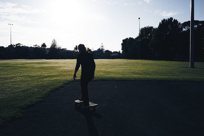 Rear view full length of woman skateboarding on field against sky