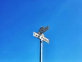 Low angle view of road sign against clear blue sky