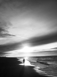 Rear view of man walking at beach against sky during sunset