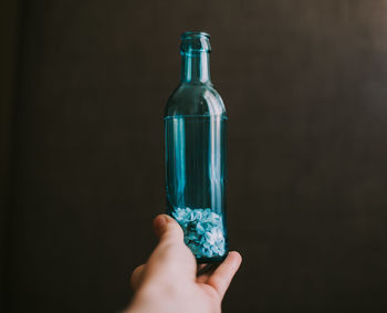 Close-up of hand holding glass bottle against black background