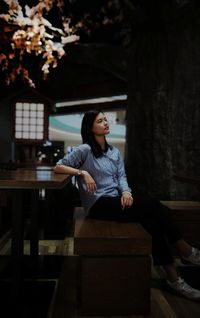 Side view of young woman looking away while sitting on bench at night