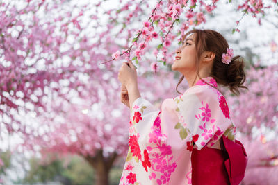Low angle view of woman standing by pink cherry blossom