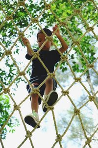Low angle view of boy climbing net