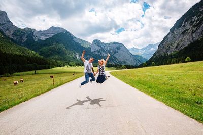 Happy couple jumping over road amidst mountains against sky