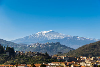 Scenic view of townscape and mountains against clear blue sky