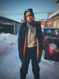 Portrait of young woman standing on snow covered road against clear sky