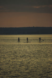 Silhouette people on beach against sky during sunset