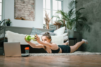 Cheerful sportsman with black hair holds the plank with dumbbells and watching