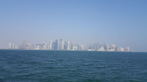 Sea by modern buildings against clear sky