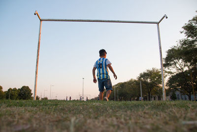 Rear view of boy on field against clear sky