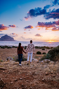 Rear view of friends standing on land against sky during sunset