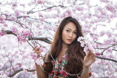Portrait of smiling young woman standing by cherry blossom