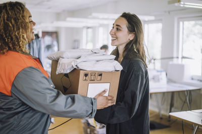 Happy fashion designer receiving package from female delivery person at workshop