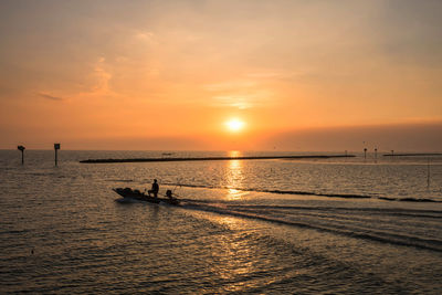 Silhouette fisherman sailing fishing boat from port at sunset of bang pu sea, samut prakan, thailand