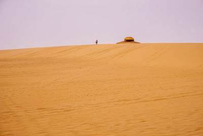 Distant view of man walking in desert against sky