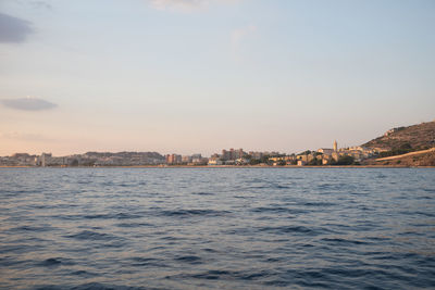 Sea by buildings against sky during sunset
