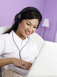 Woman listening music on headphones while using laptop at home