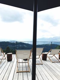 Empty chairs and table by sea against sky