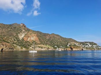 Scenic view of sea by mountain against sky