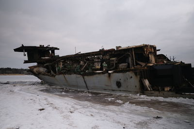 Abandoned boat on shore by sea against sky