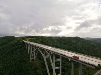 Bridge over green mountain against cloudy sky