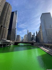 Buildings by city against sky green river